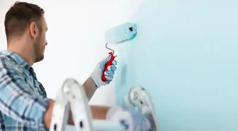 Application minutieuse de peinture lessivable lavable sur un mur par un peintre professionnel, assurant une finition lisse